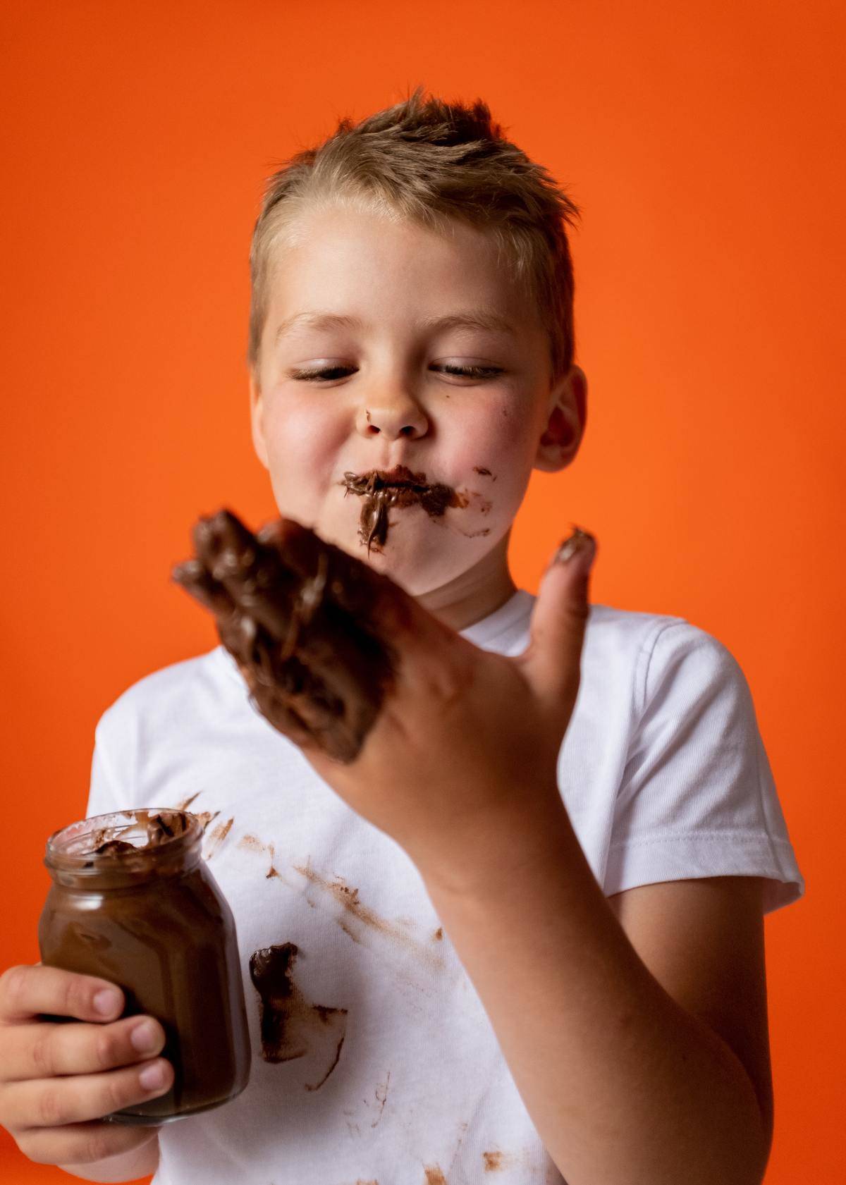 boy in white shirt covered in chocolate on hands and face