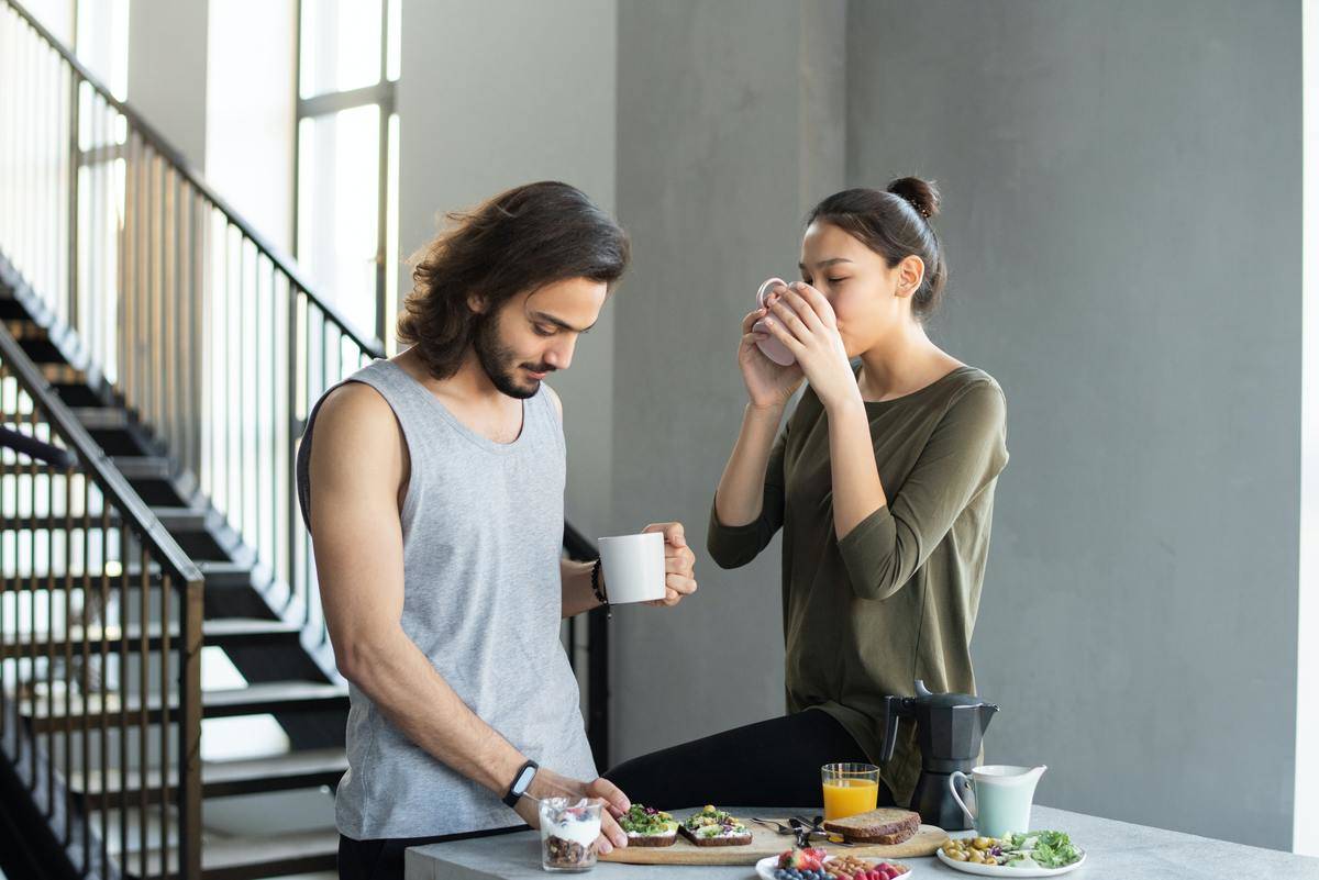 man and woman standing drinking coffee eating at home