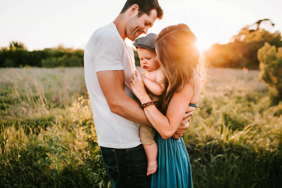 mother and father hold baby in field
