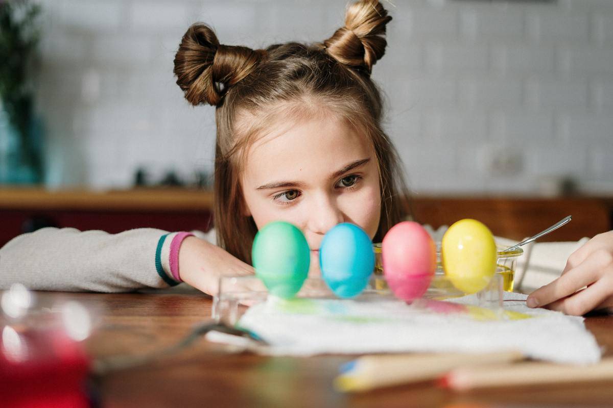 girl looking at painted eggs on table