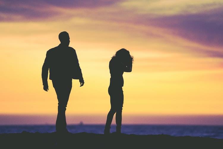 sunset silhouette photo of woman with her head in her hands and a man walking toward her