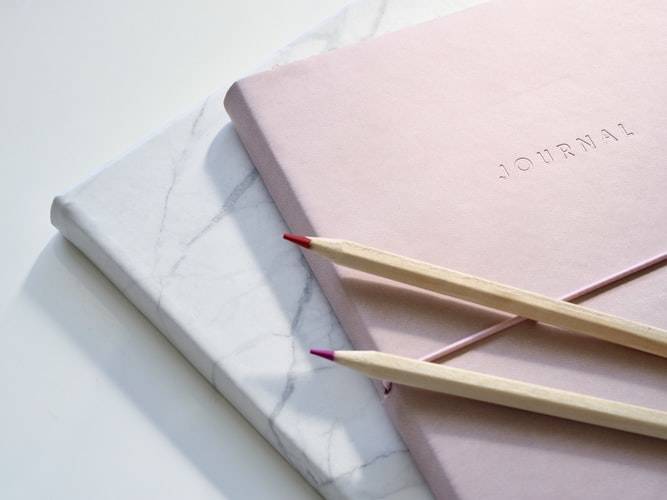 light pink journal atop a marble-patterned journal with pencil crayons