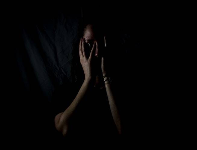 woman with hands over her face and eyes photographed in dark space