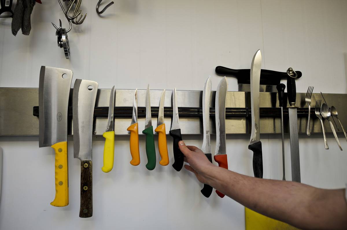 A butcher reaches for a knife hanging on a magnetic knife strip.