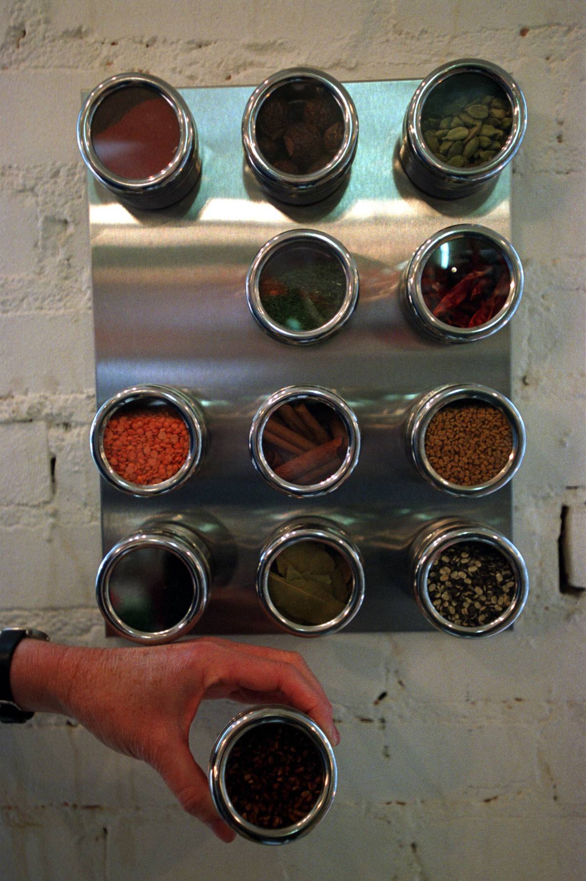 A person takes a stainless steel spice container off of a magnetic mounted spice rack.