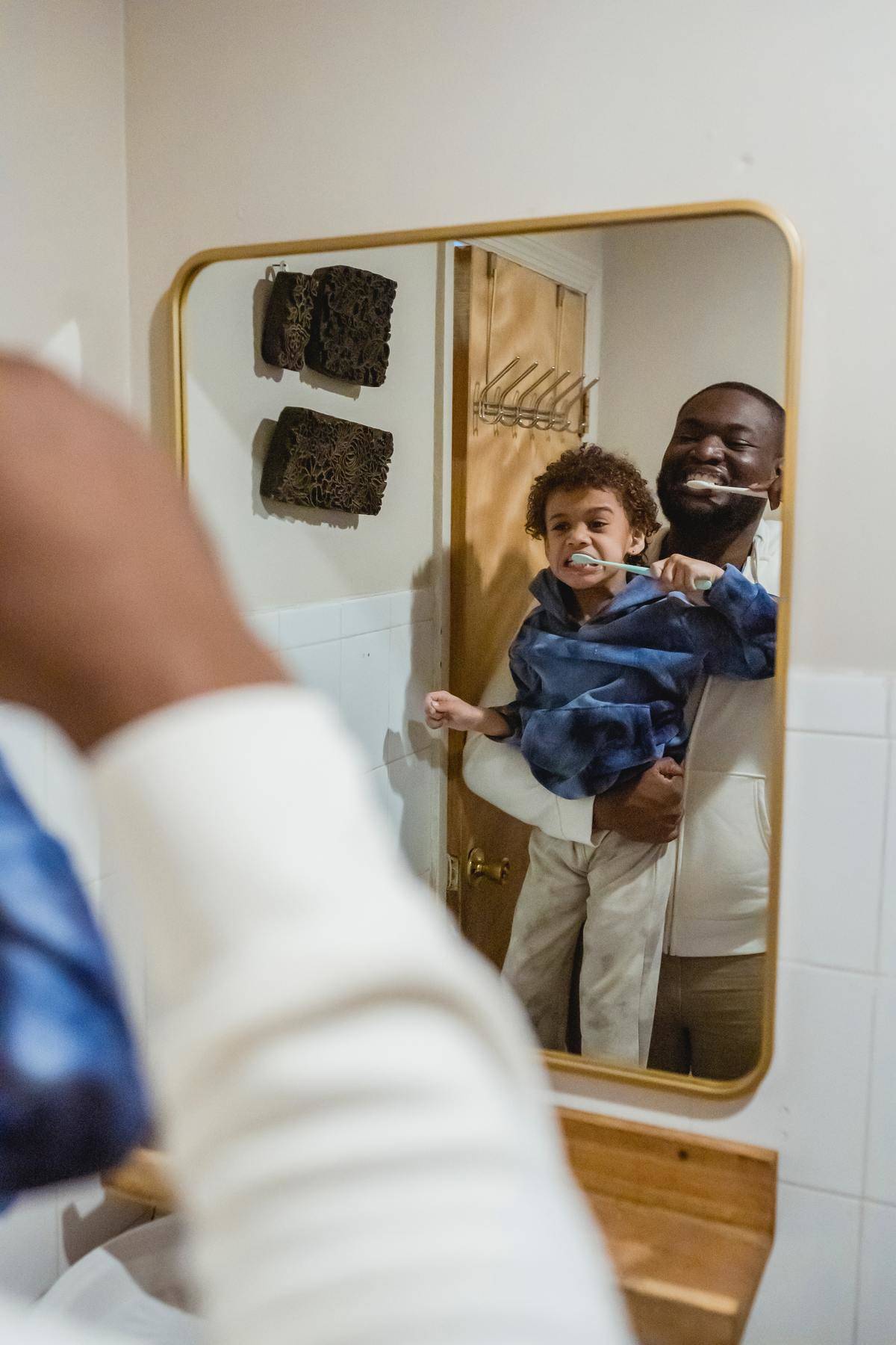 man holding up child to mirror as they brush their teeth