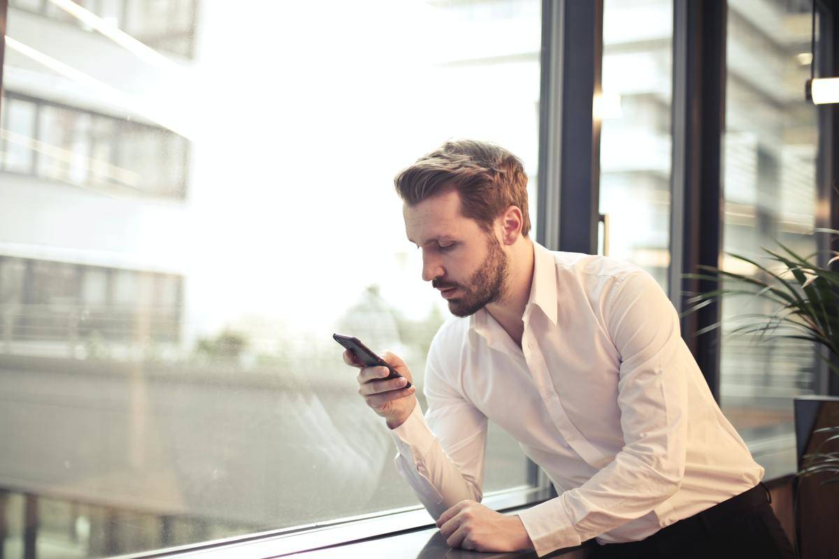 man checking his phone by the window in office