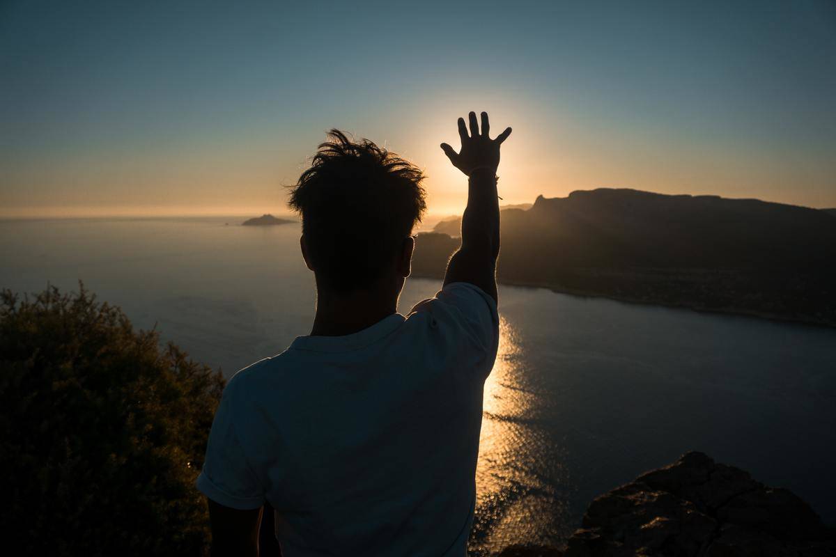 man reaching for the sun over the water