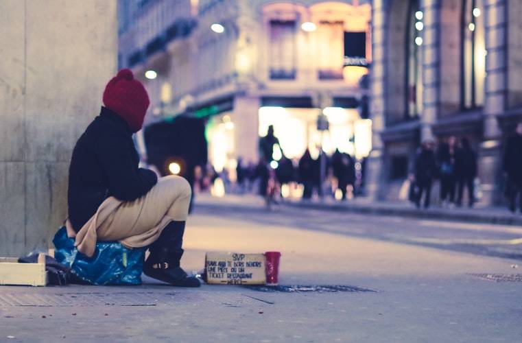 Person sitting on street in winter clothes with sign in front of them