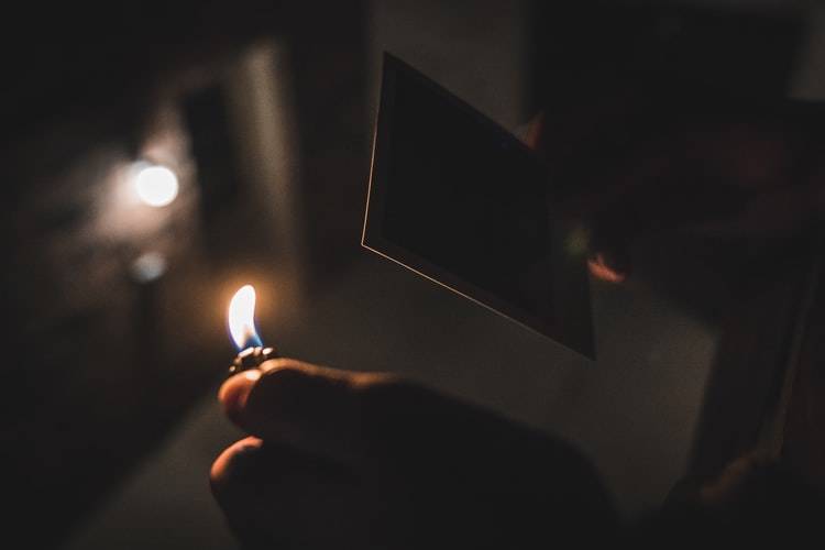 dark image of someone lighting a polaroid picture on fire 