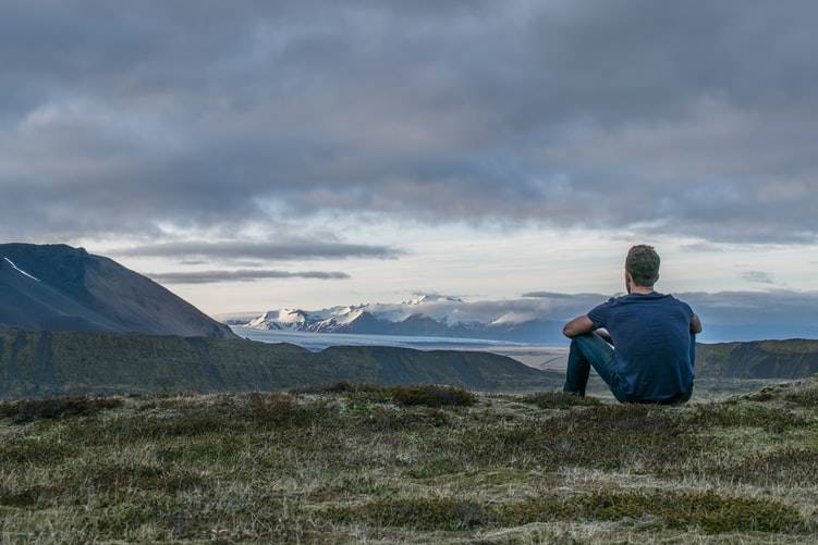 man sitting alone on a hill against a beautiful mountain scene 