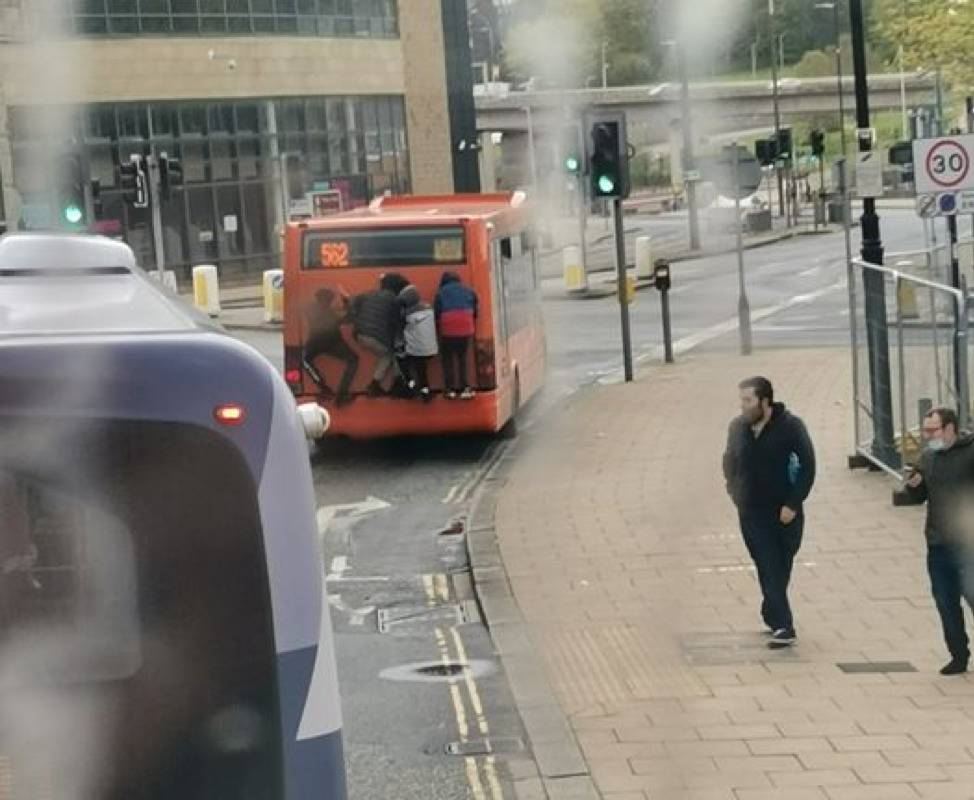 four people secretly riding on the back of the exterior of a bus