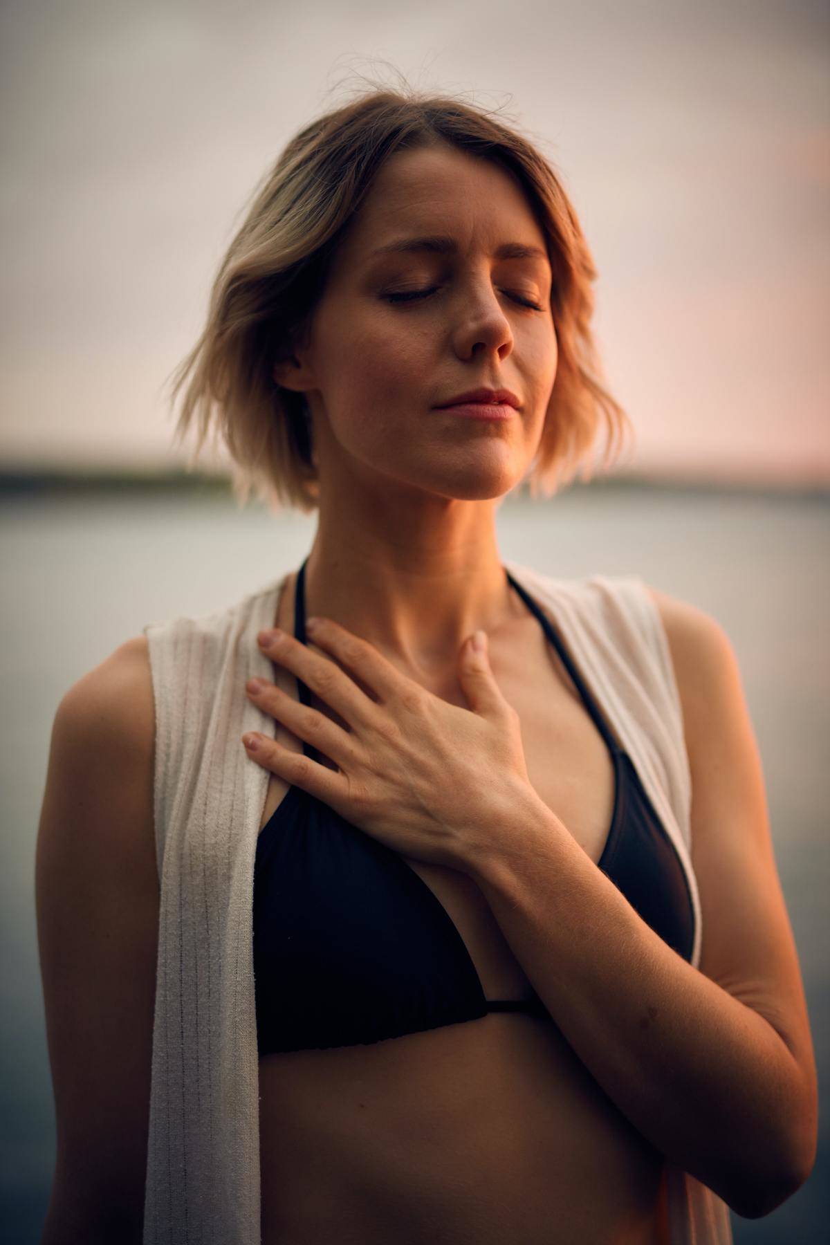woman closes her eyes at the beach with her hand on her chest
