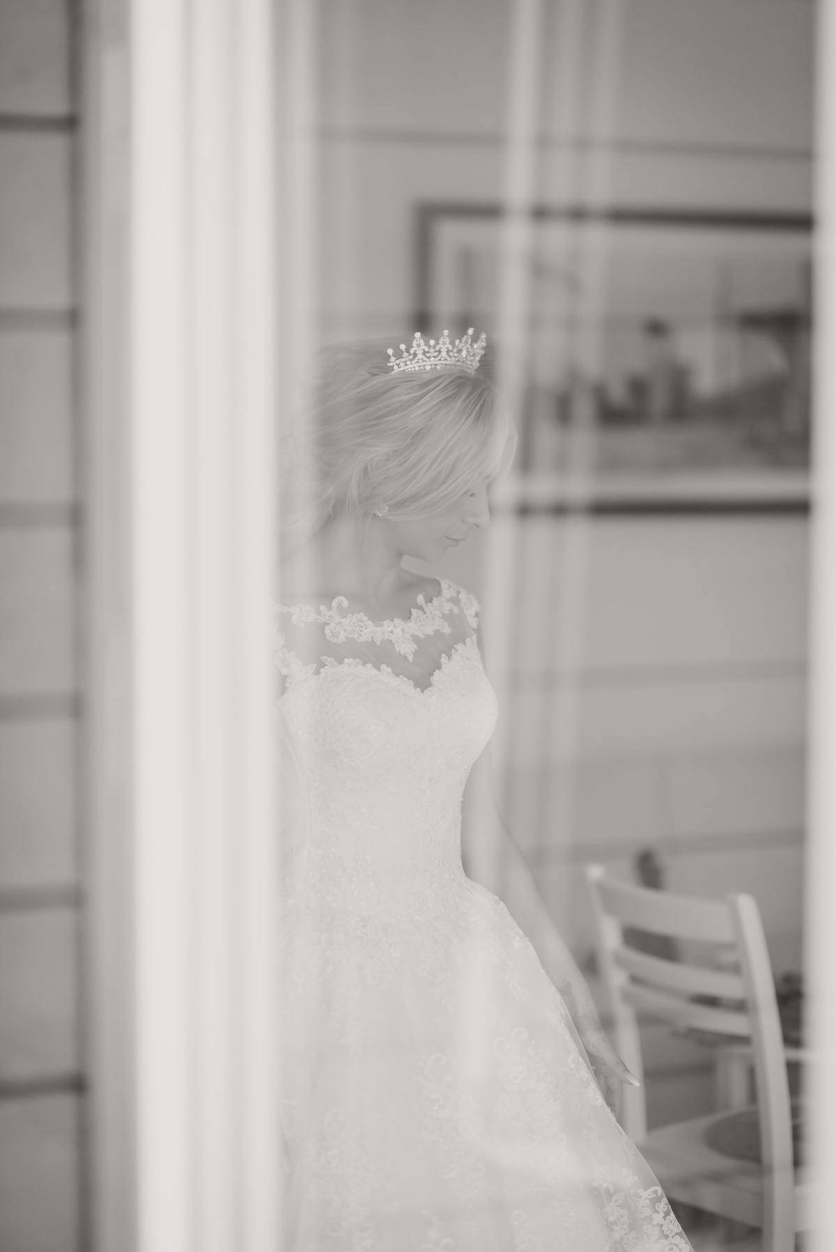 woman in wedding dress view through curtained window