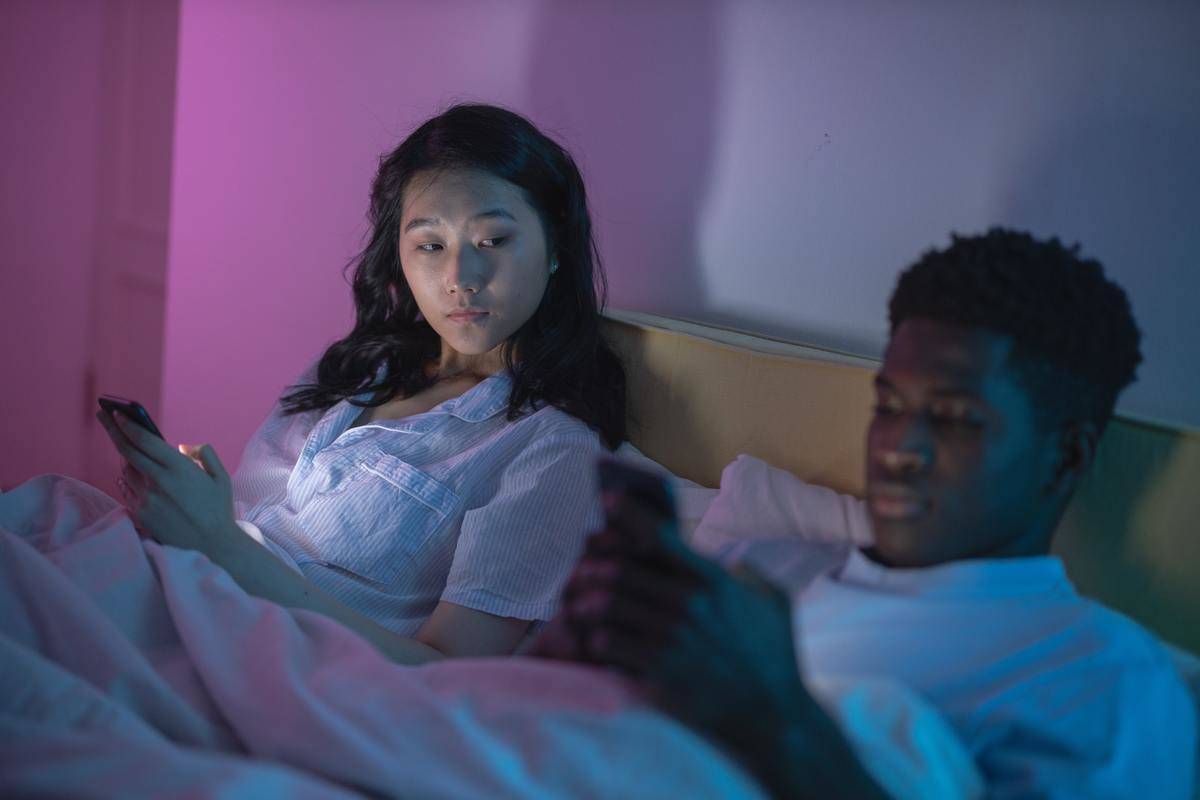 woman looking over at man as they text in bed