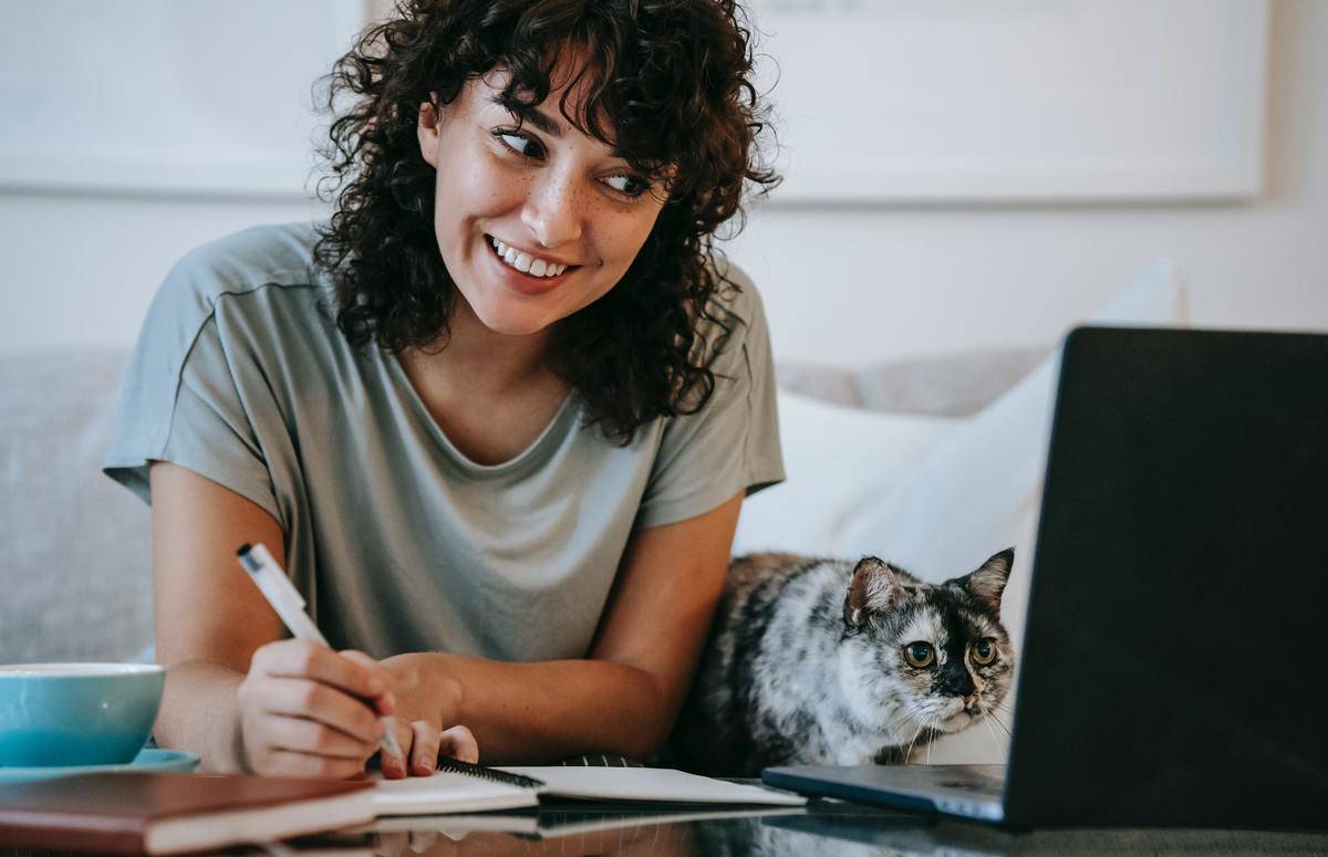 woman working on laptop with cat next to her