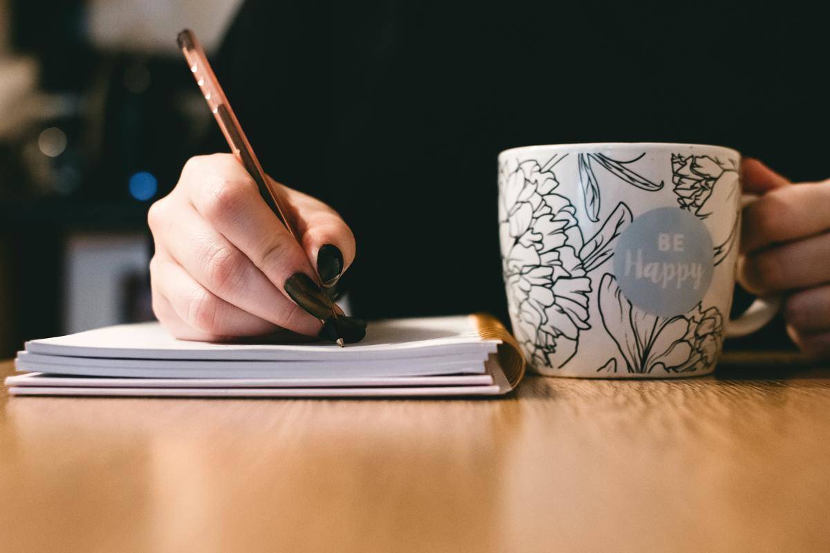 woman writing in journal beside mug
