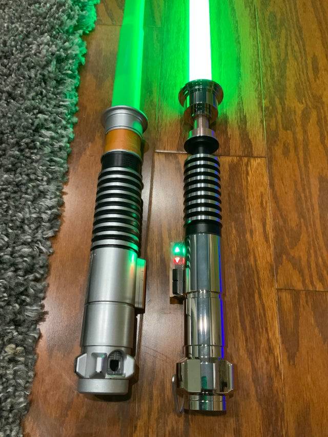 Two lightsabers glowing green, left one $10 is cheaply made with plastic, the $400 one on the right is metal and high tech