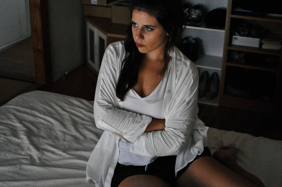 Woman sits on bed and looks angry