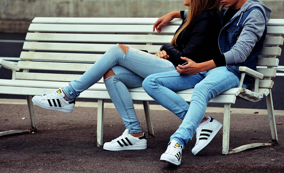 Couple sit on park bench wearing similar jeans and same shoes