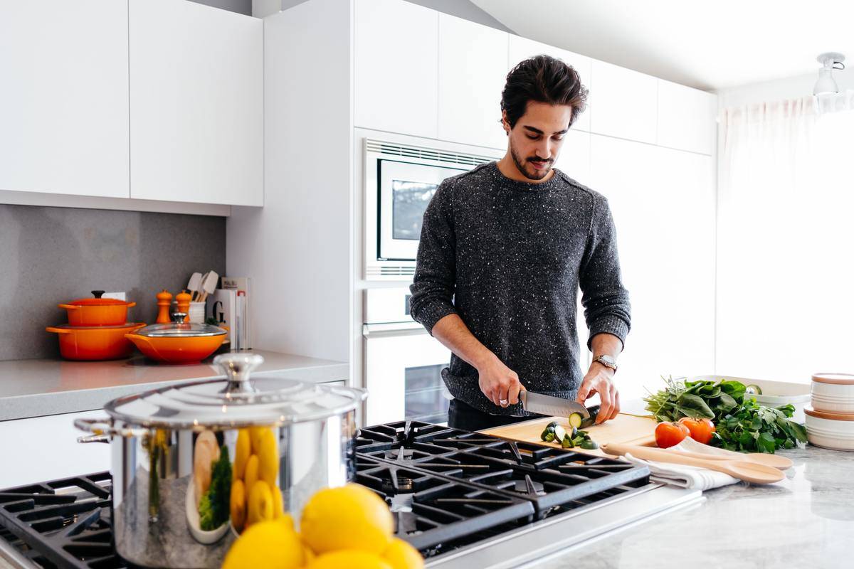 Tall man in grey shirt cuts vegetables in a home kitchen