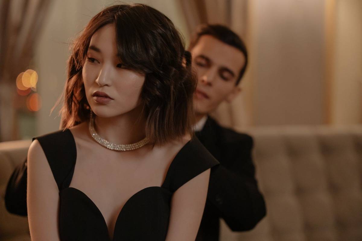 woman looking suspicious as a man puts on her necklace for her