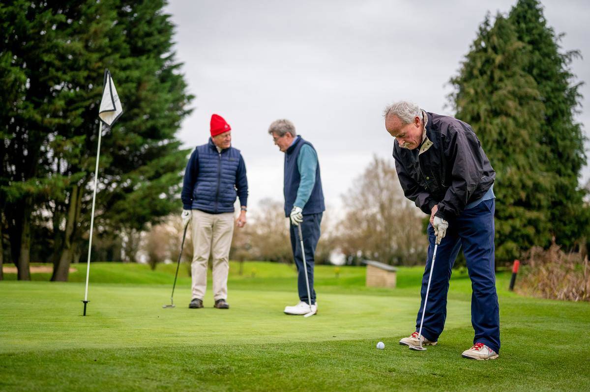 Group of senior men golfing, two men discuss while the third lines up his putt