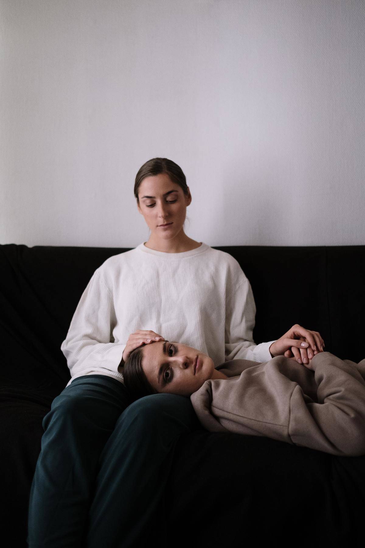 Two women sit on couch looking solemn/quiet