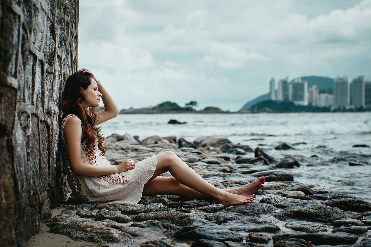 Woman sits alone on beach and stares off at the ocean 