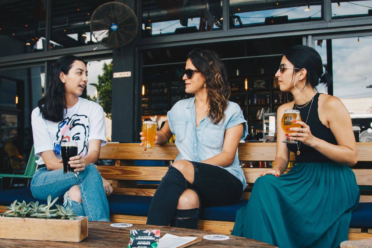 Three women socialize on patio holding beers