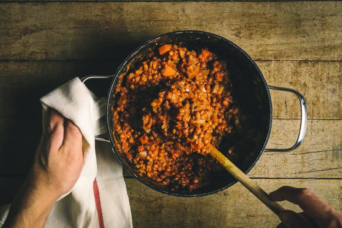 A chef stirs around cooked lentils in a pot.