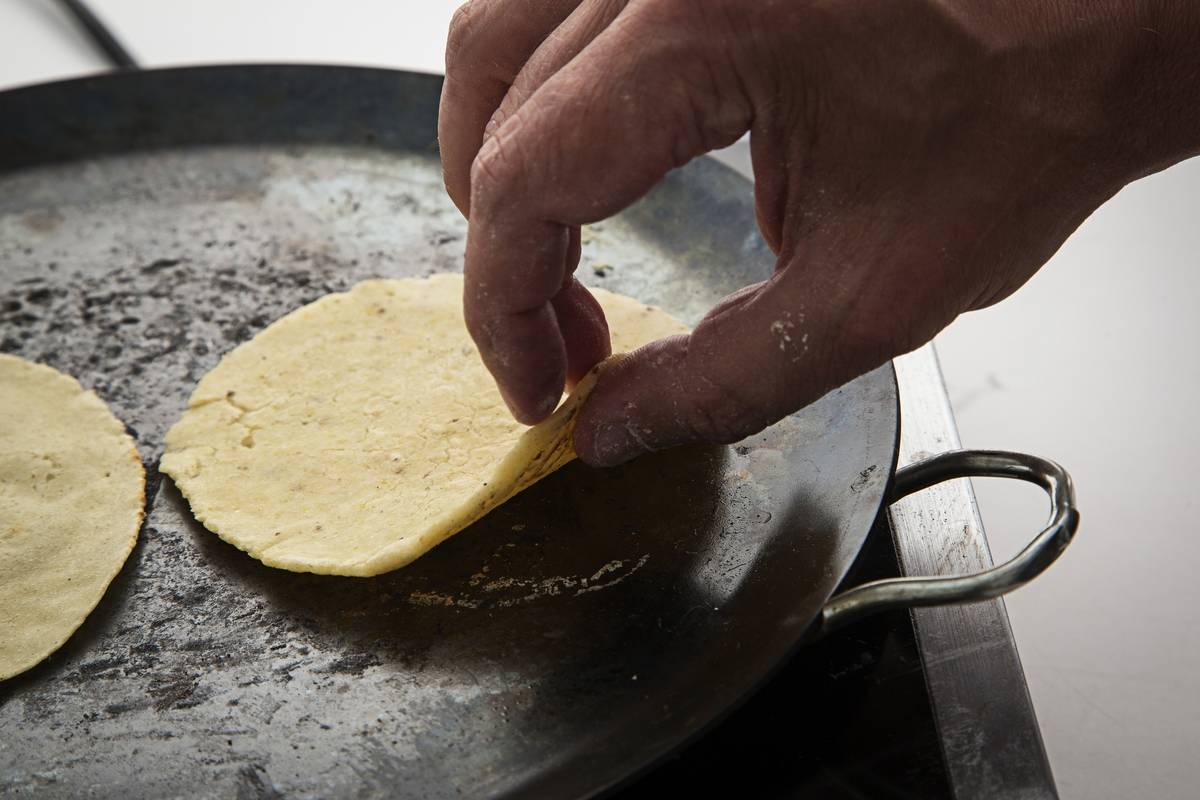 A man lifts a corn tortilla from a pan.