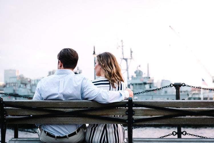 back shot of couple sitting on park bench, the woman is looking at the man but he is looking away