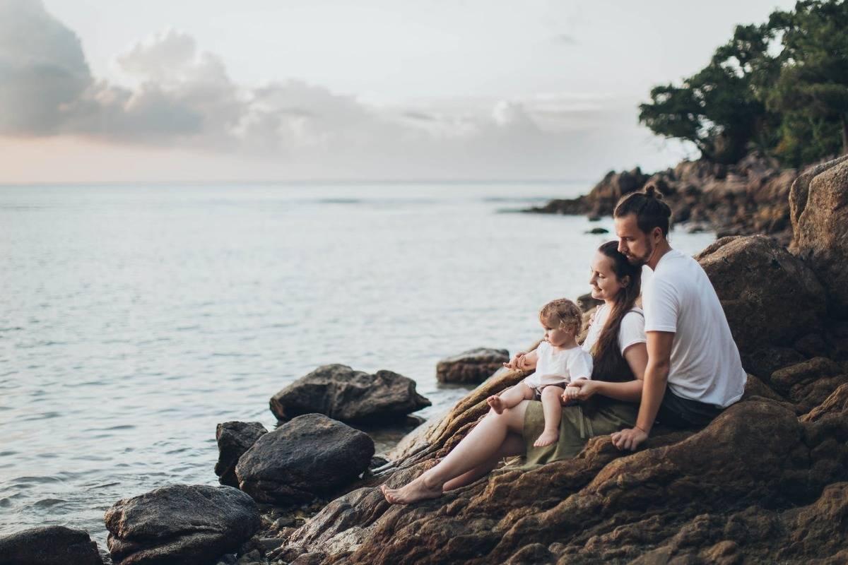 couple and kid sitting on rocks looking out at the water