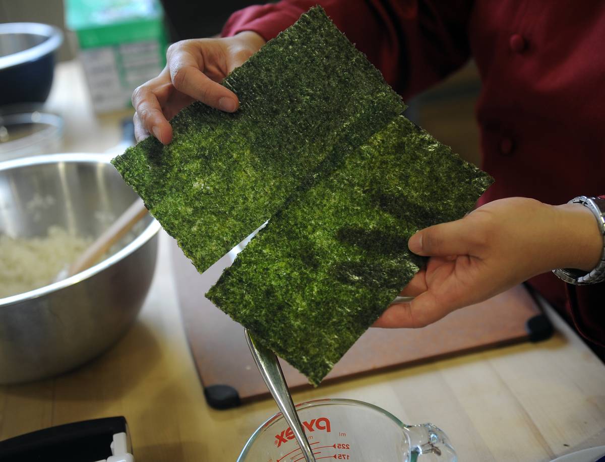A chef holds two roasted seaweed sheets.