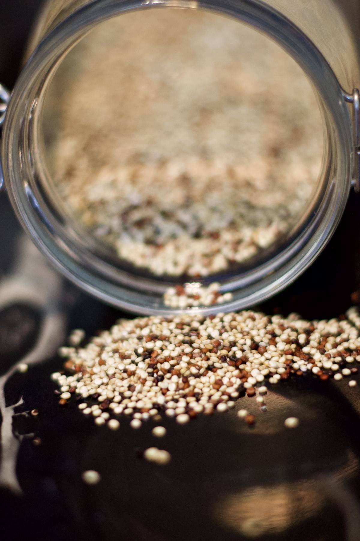 Dried quinoa pours out of a glass jar.