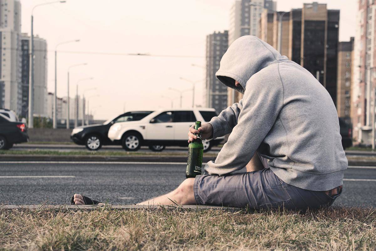 man having a beer on the ground on the street
