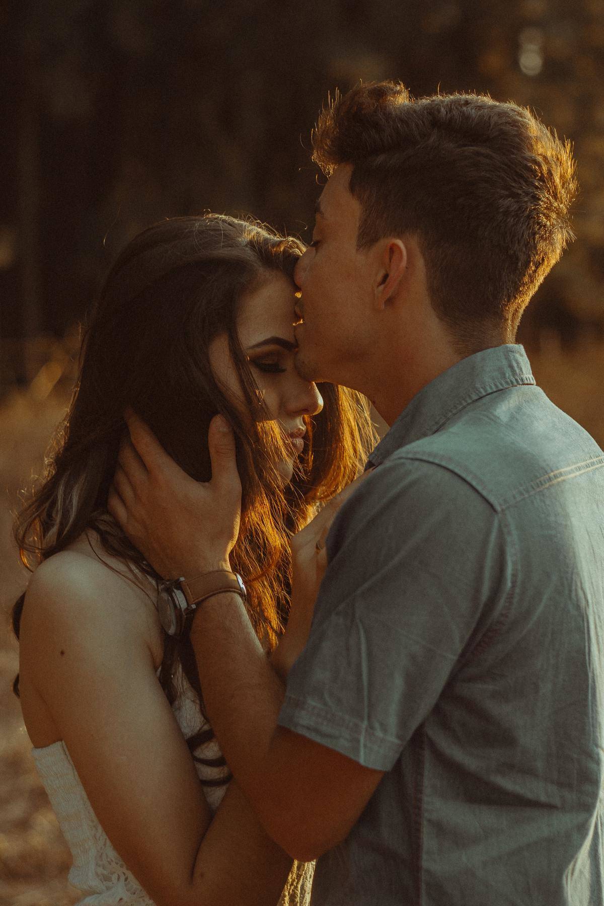man kissing woman's forehead in a field
