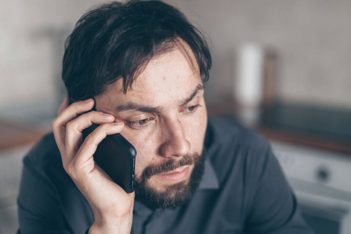 man seated holding up black phone to ear
