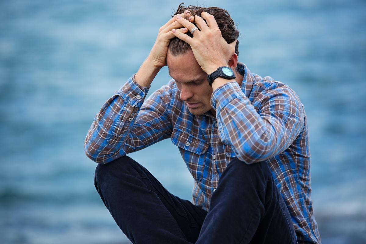 man sits by the water pushing his hair up