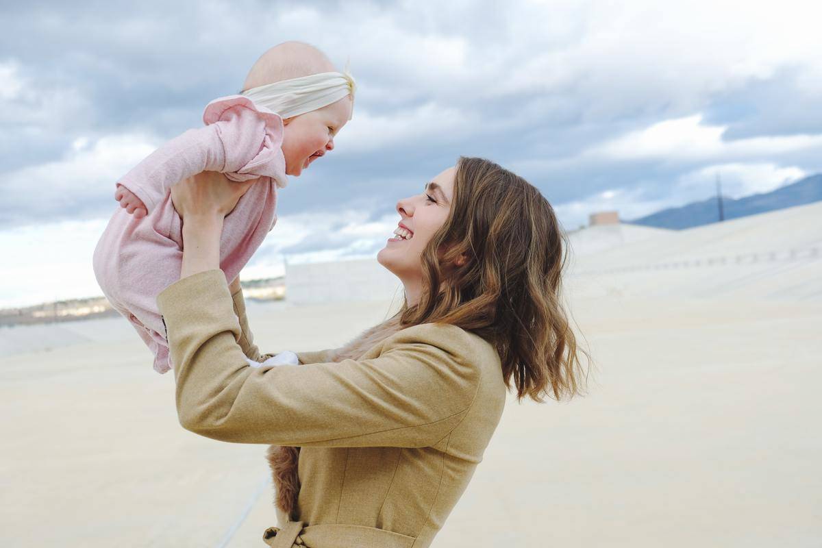 mom holds up baby at the beach
