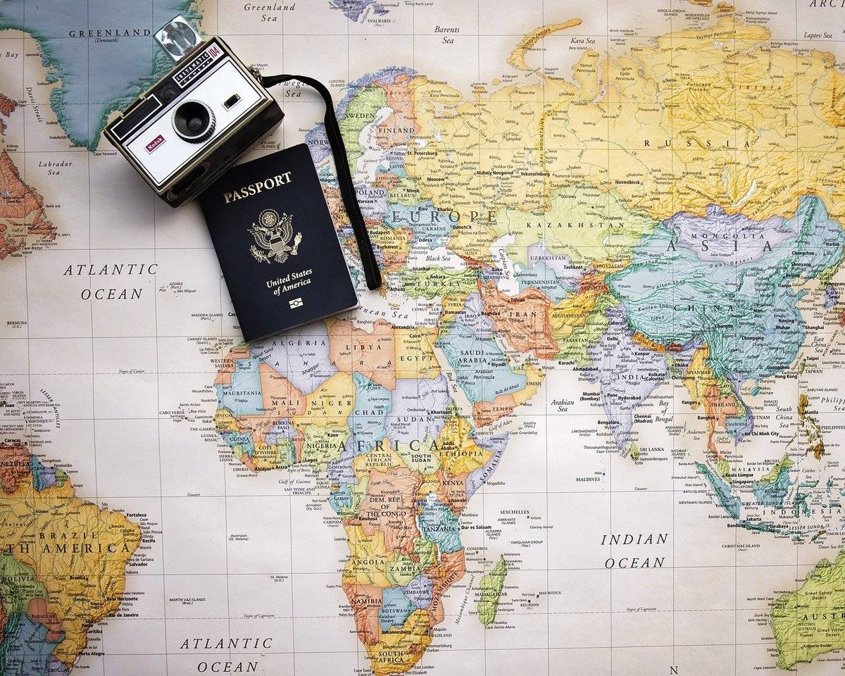 A camera and passport are on top of a paper map of the world.