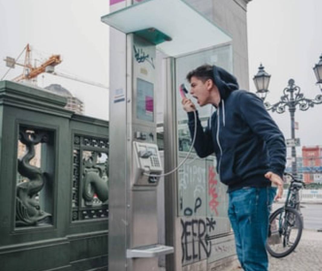 man screaming into payphone