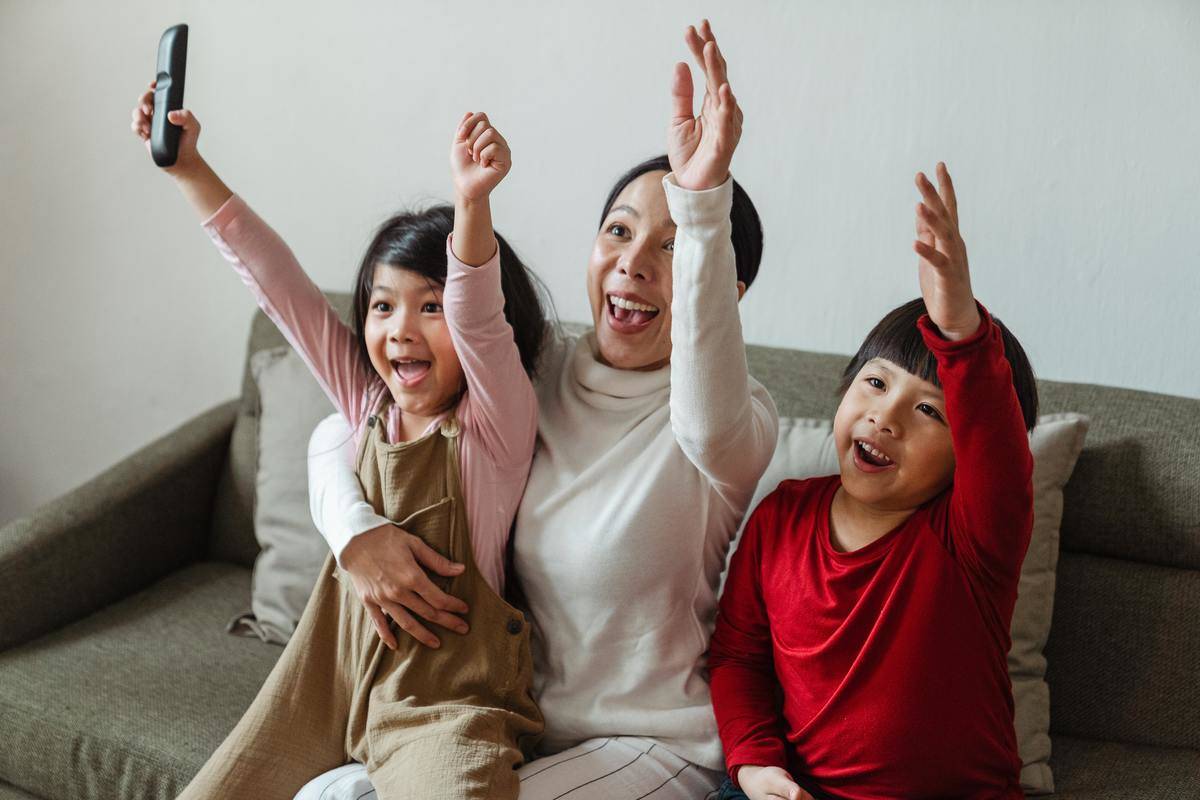 woman seated with two kids on couch hands raised
