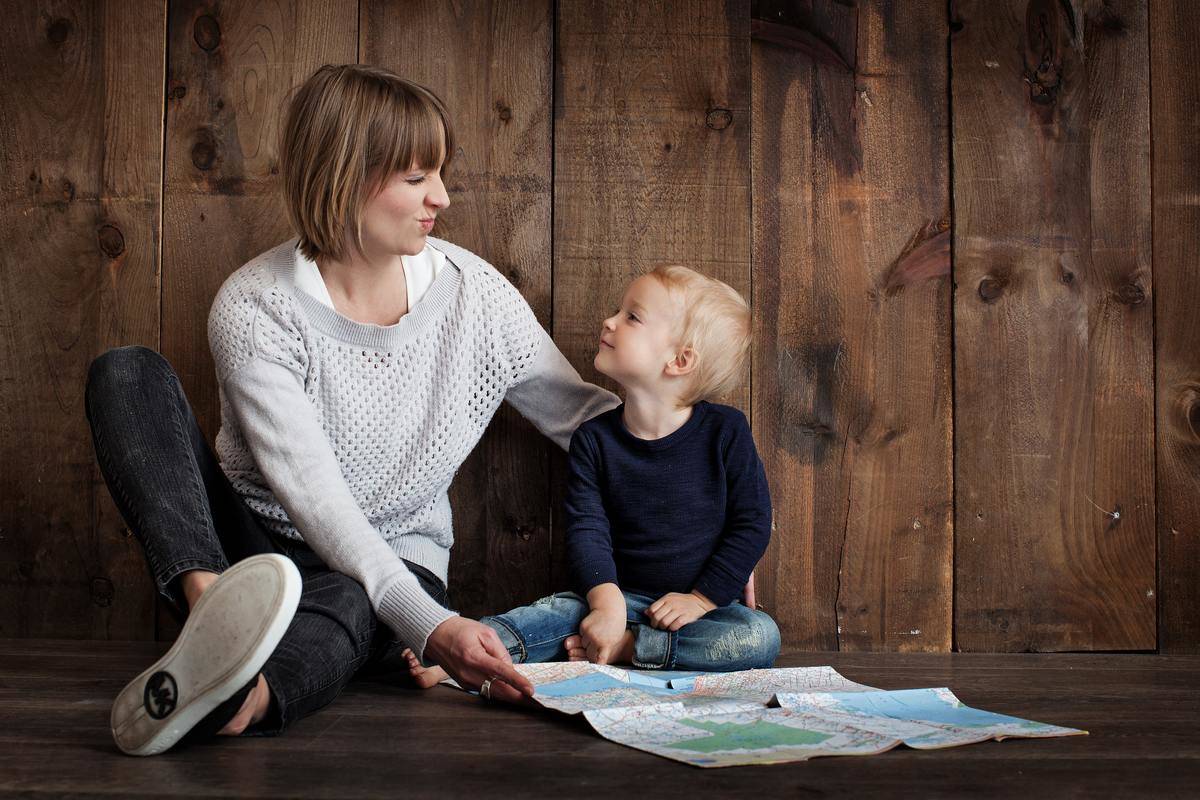 woman in knit sweater seated making faces at little boy