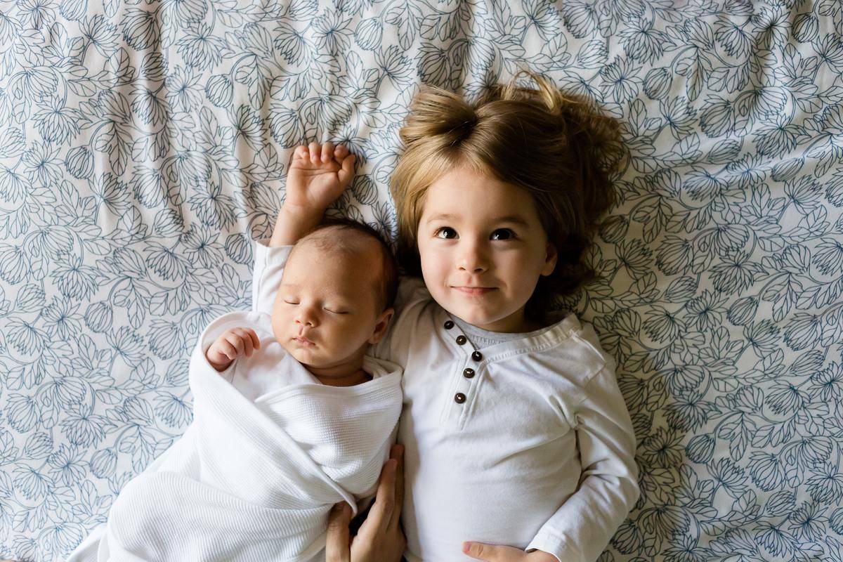 little girl and baby lying on white bed spread