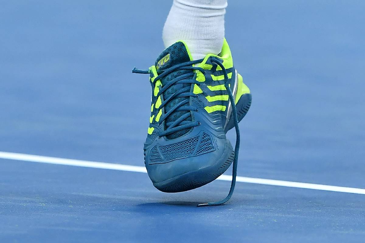 A broken shoelace is seen under a tennis player's shoe.