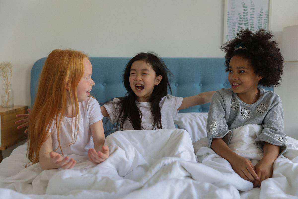 three girls laughing sitting on bed