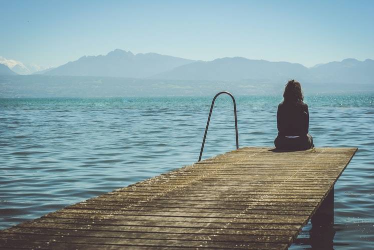 woman sitting alone by water on dock