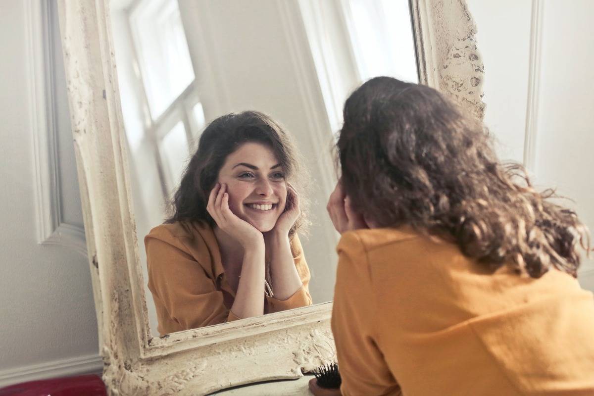 woman staring at herself in the mirror and smiling